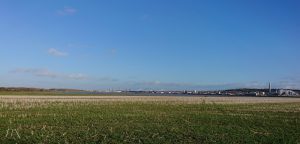 Blue sky and green stubble fields with bridges and industrial buildings in the background